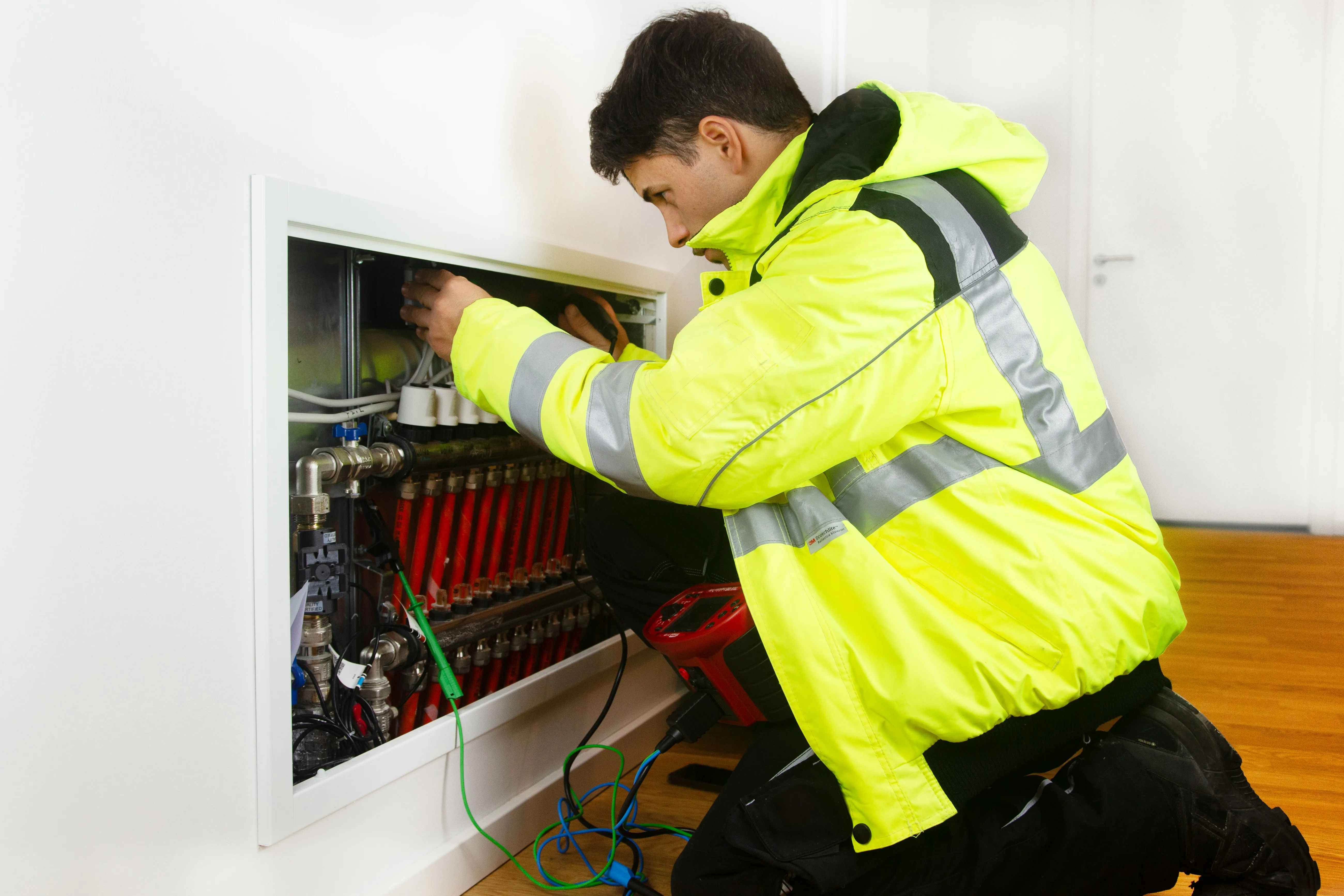 Engineer in hi-vis working on a heating-system distribution manifold during a heat pump installation