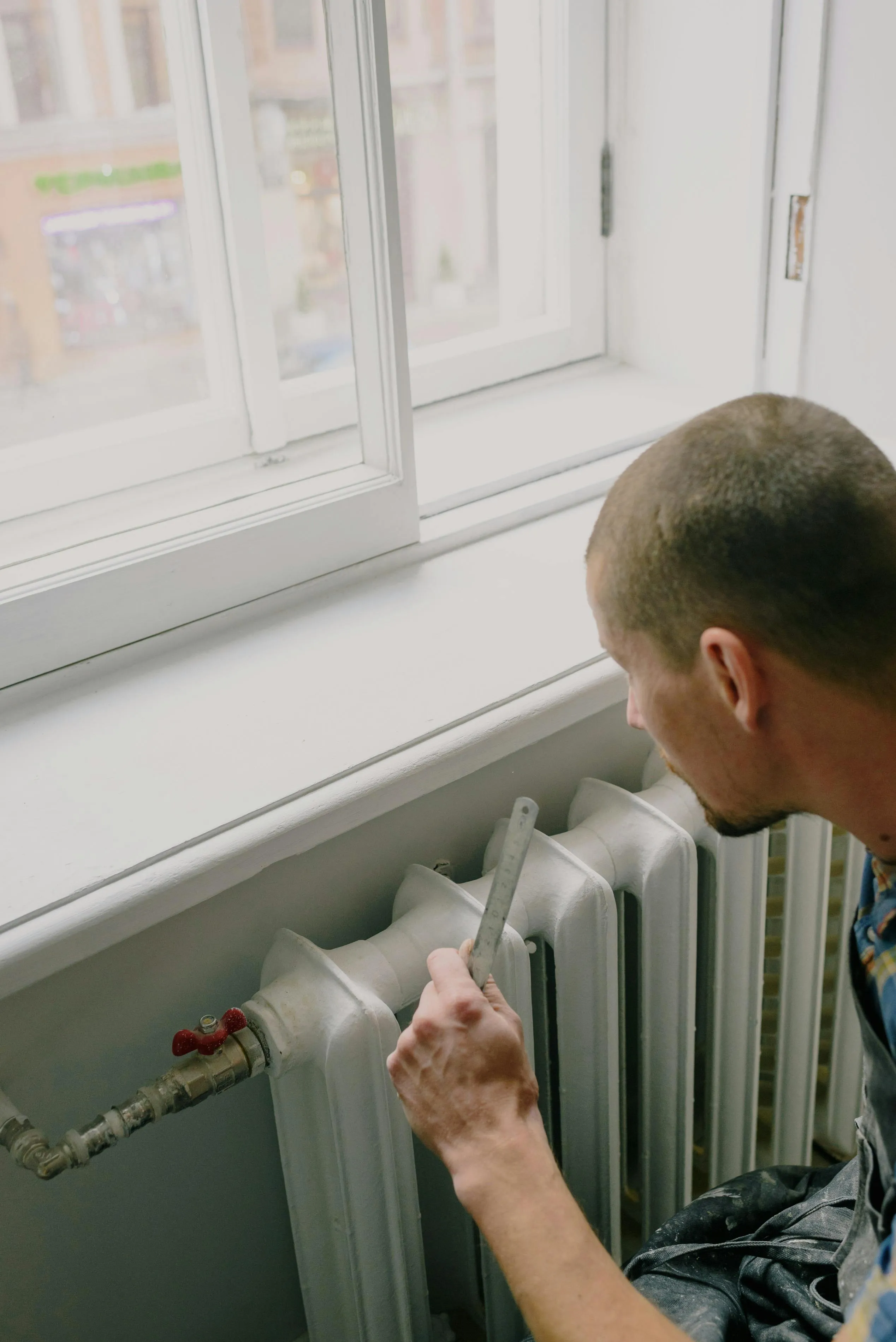 Engineer measuring an indoor radiator with a folding rule — heat-loss assessment includes per-room emitter capacity